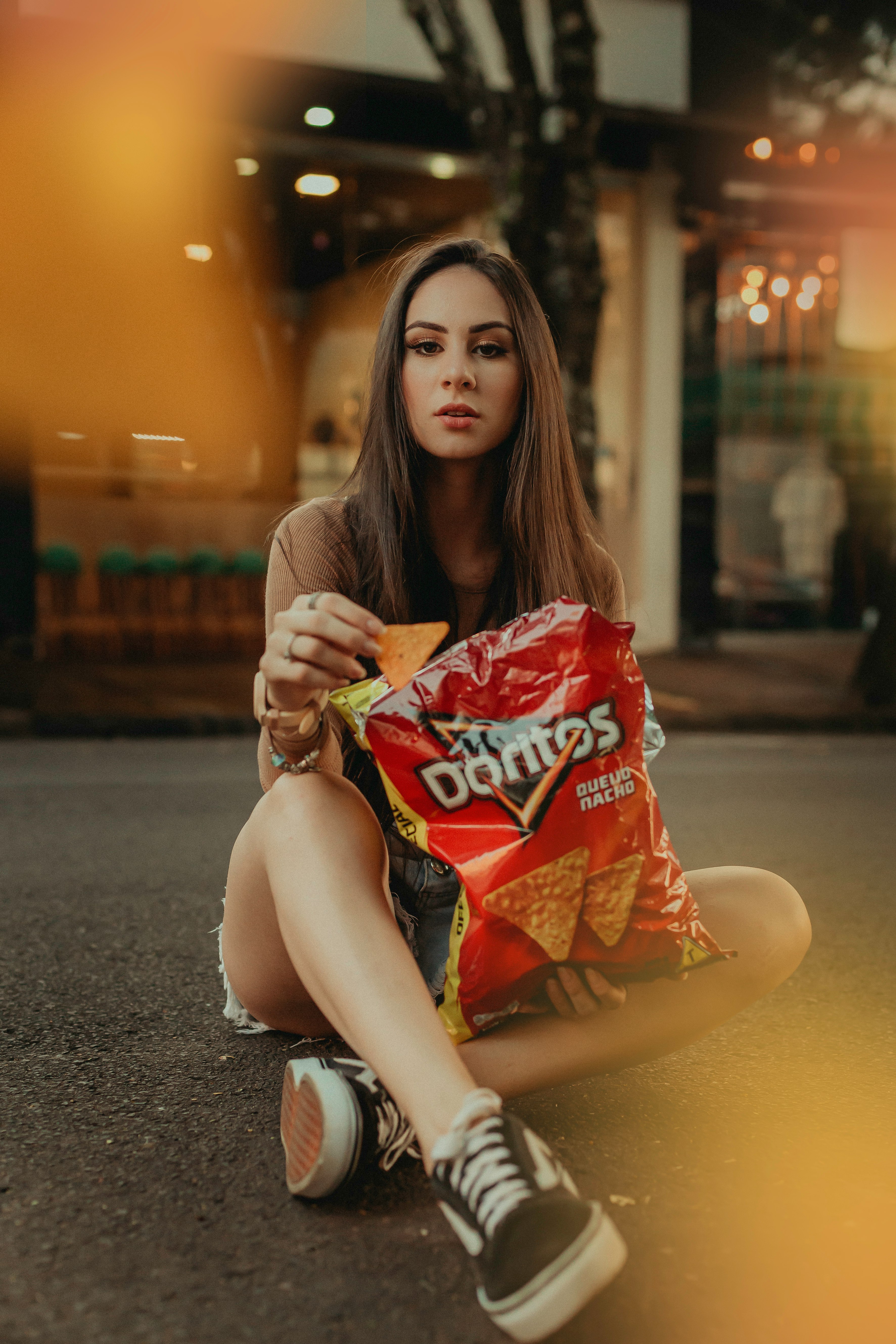 woman in brown shirt sitting on the street holding red and white plastic pack during daytime